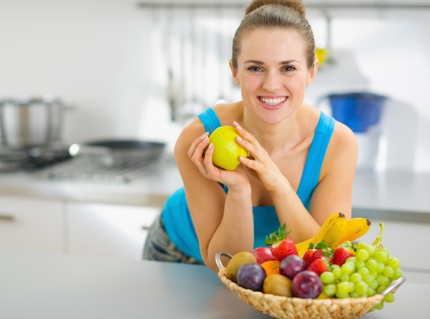 Smiling young woman holding apple in modern kitchen
