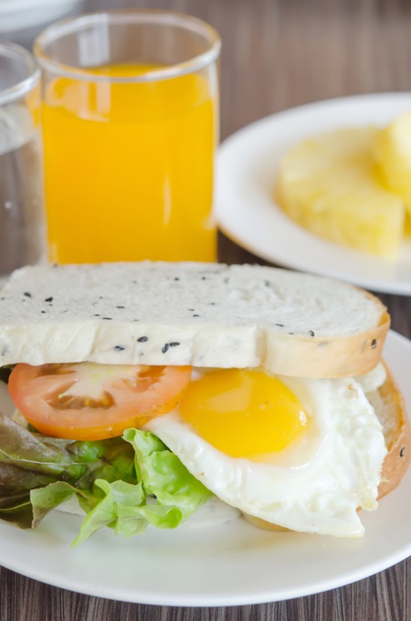 fresh sandwich with tomatoes , lettuce and fried egg on dish with juice